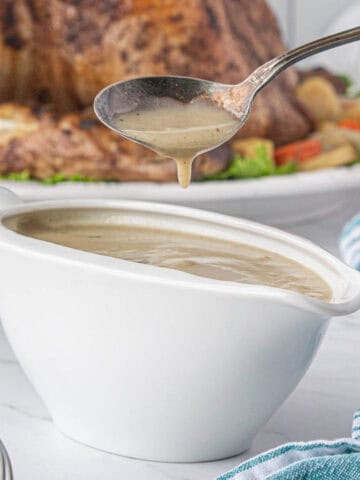 Homemade gravy in a gravy boat, with a spoon dipping out some gravy.