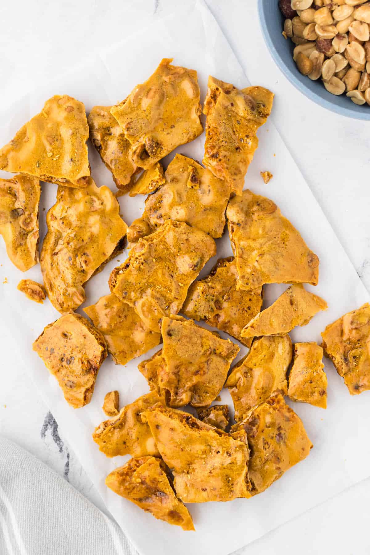 Freshly made microwave peanut brittle broken and laying on parchment paper.