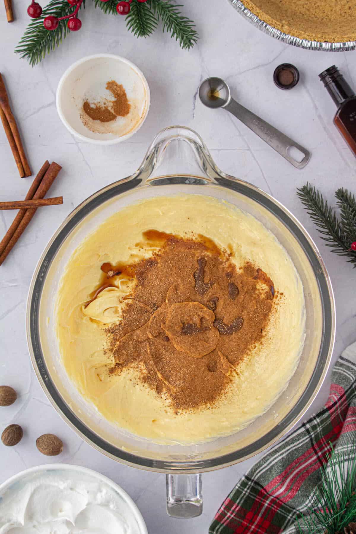 Cinammon and nutmeg added to the creamy eggnog mixture in a mixing bowl.