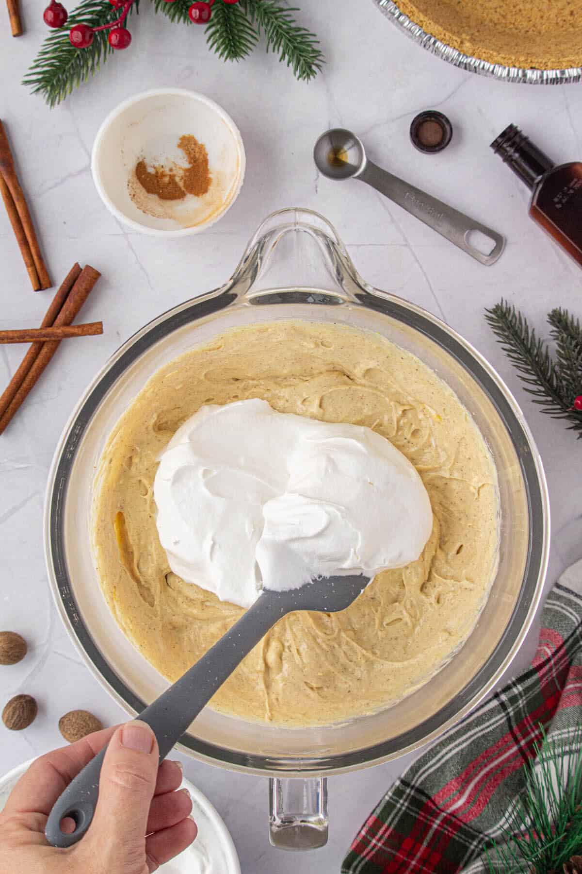 Cool Whip being folded into the eggnog mixture with a spatula.