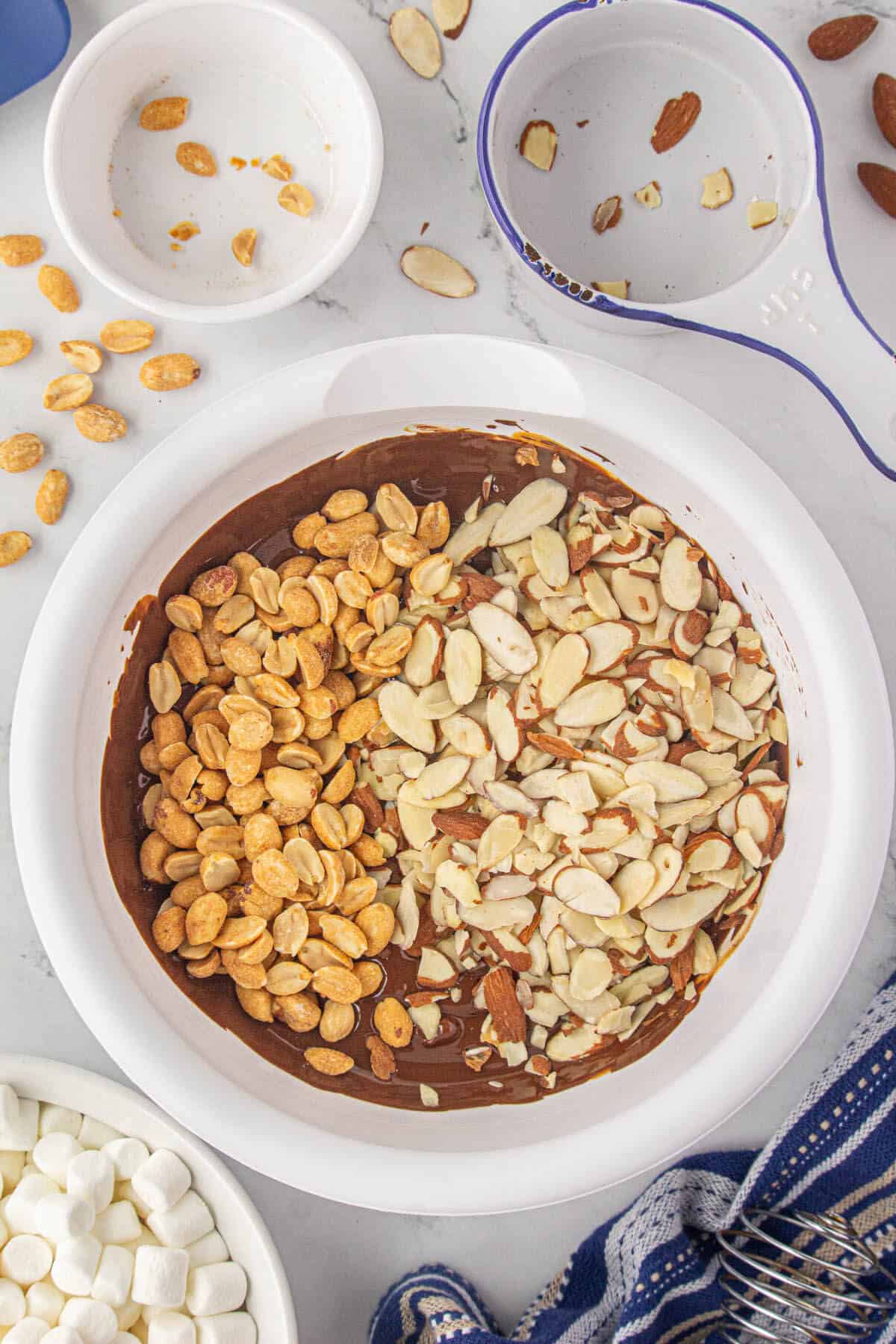 Peanuts and sliced almonds in abowl of melted chocolate.