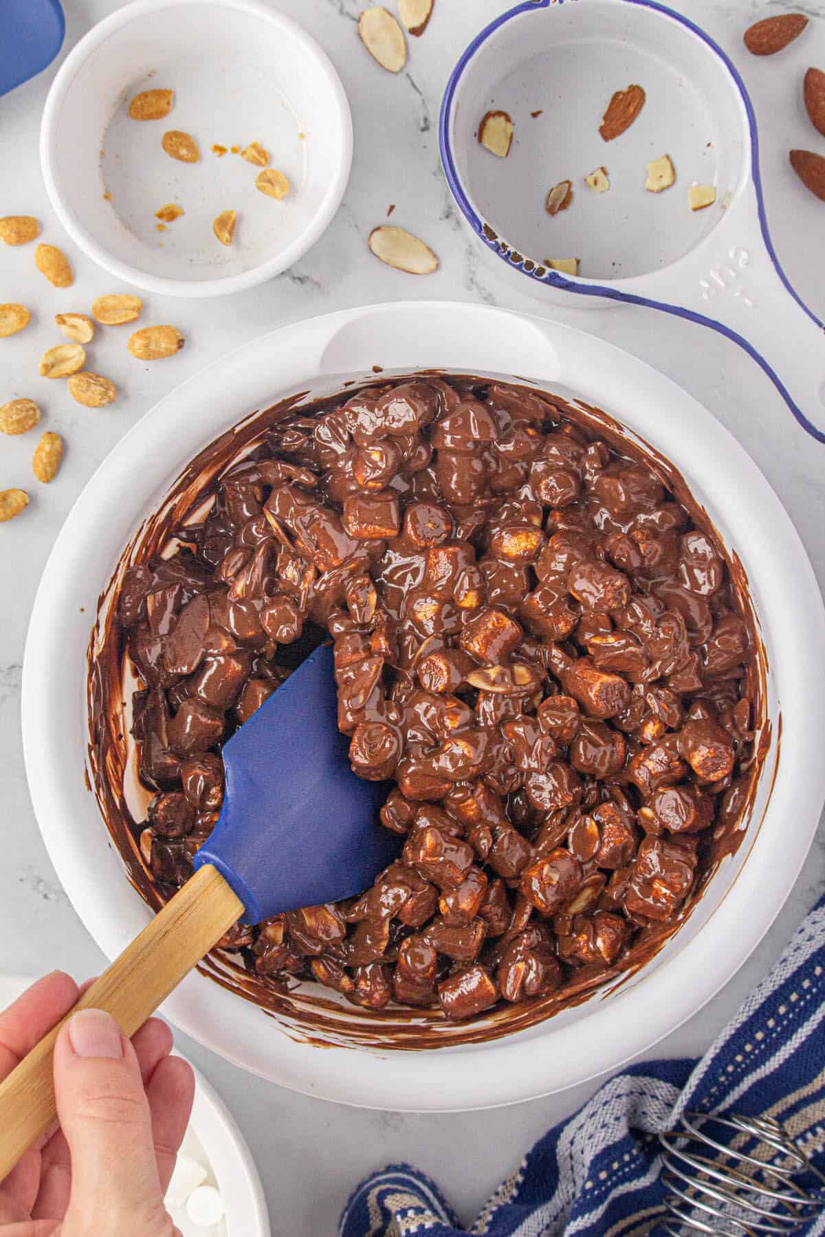 Almonds, peanuts and marshmallows in a bowl all mixed together with a spatula.