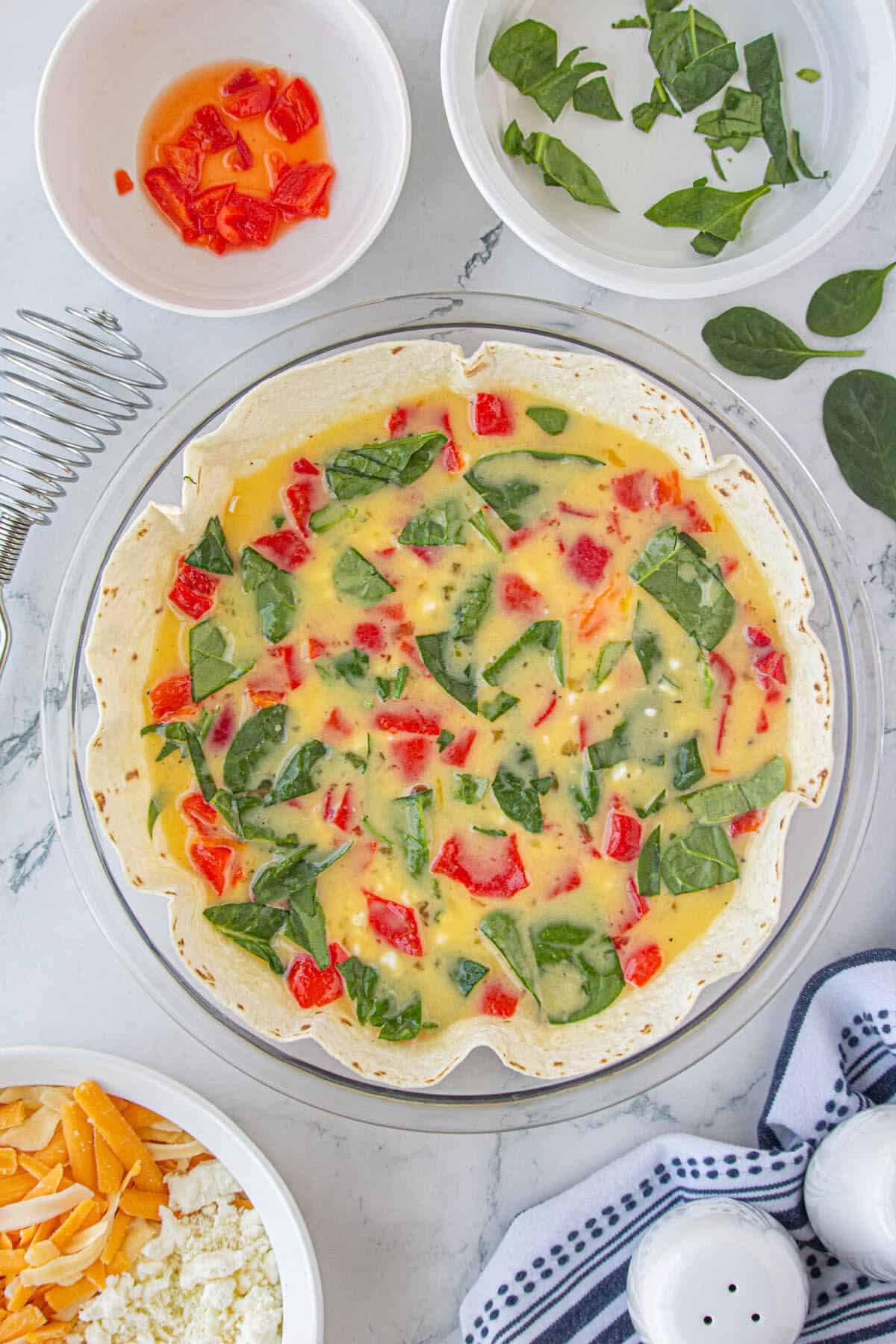 Red bell peppers and chopped fresh spinach sprinkled over tortilla quiche before baking.