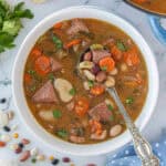 15 bean soup with ham in a white bowl with a serving spoon.