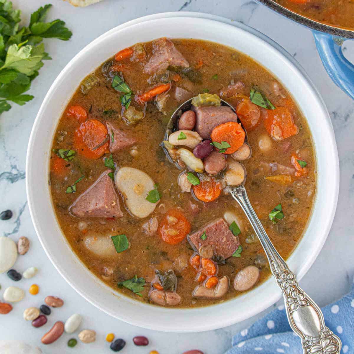 15 bean soup with ham in a white bowl with a serving spoon.