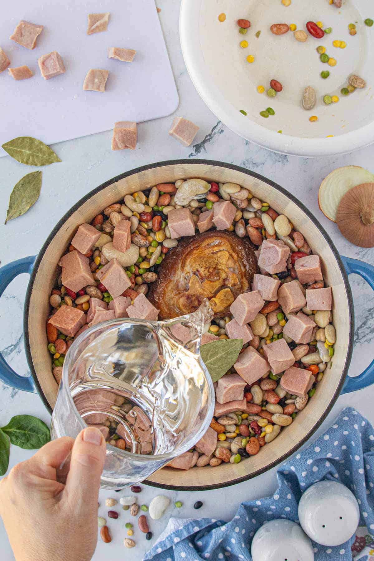 Water pouring into a stock pot filled with beans and ham.