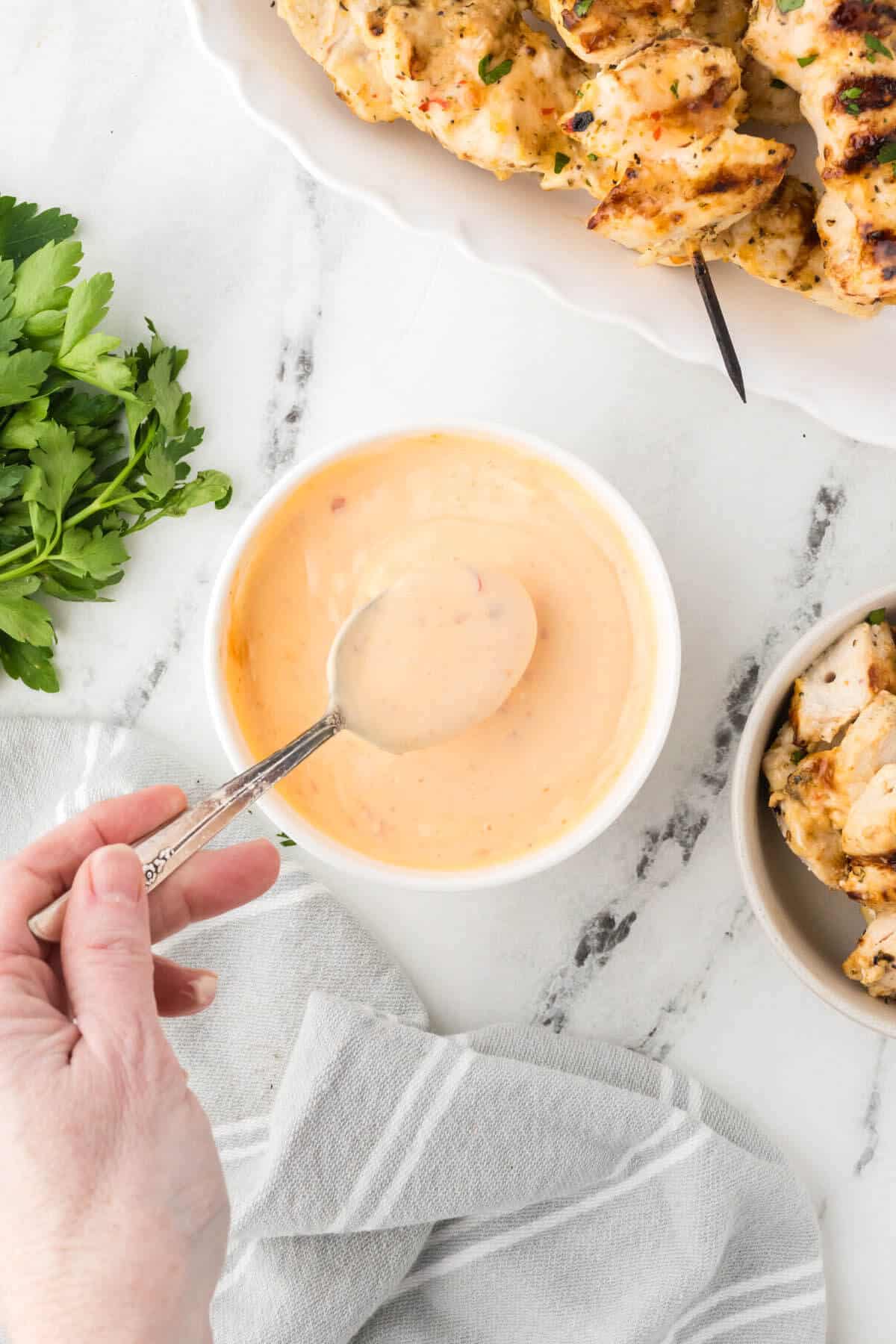 Bang bang dipping sauce in a bowl, with a spoon scooping out some to drizzle over grilled chicken.