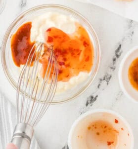 Whisking a creamy mayonnaise based sauce in a bowl.