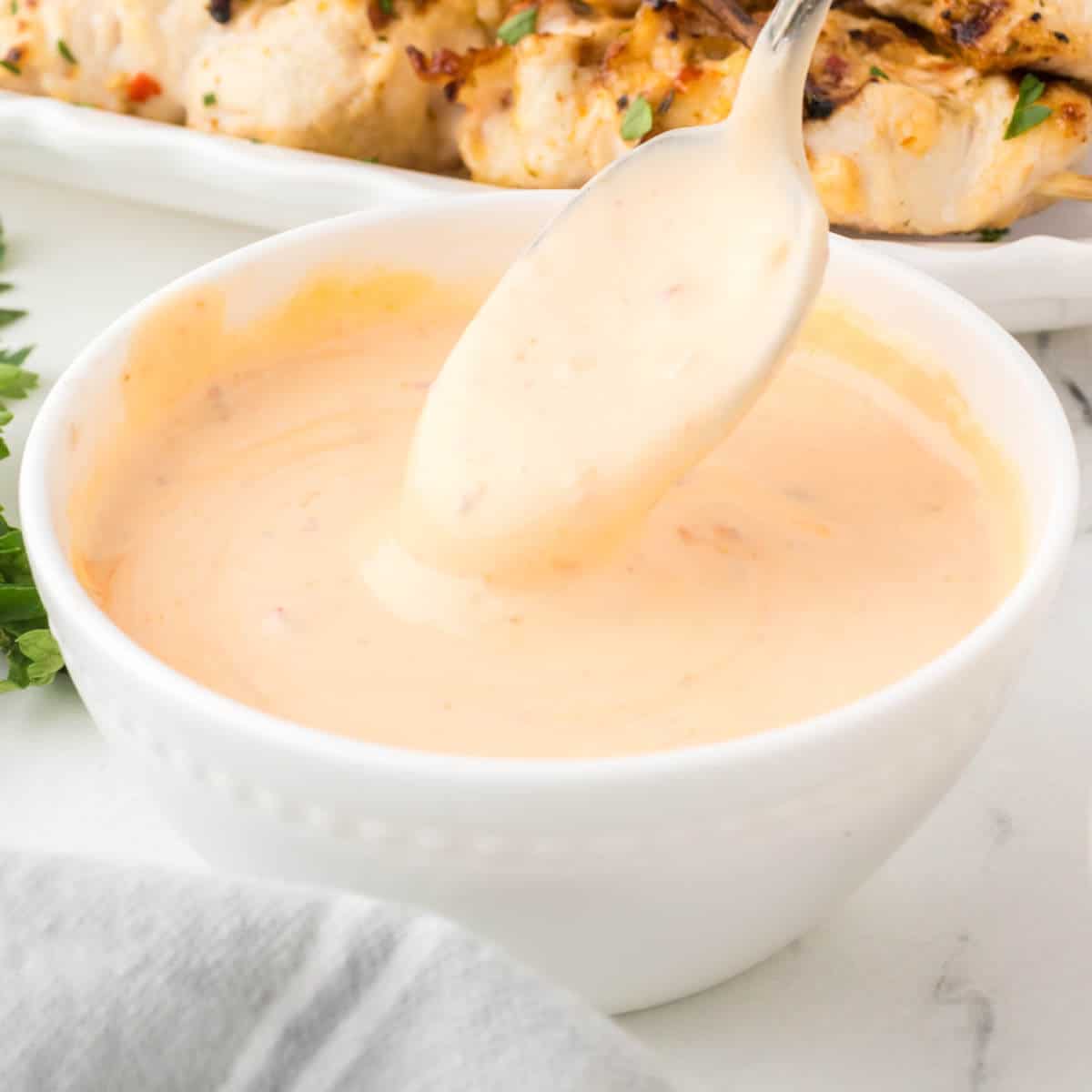 Bang bang sauce in a white bowl with a spoon dipping into the sauce.