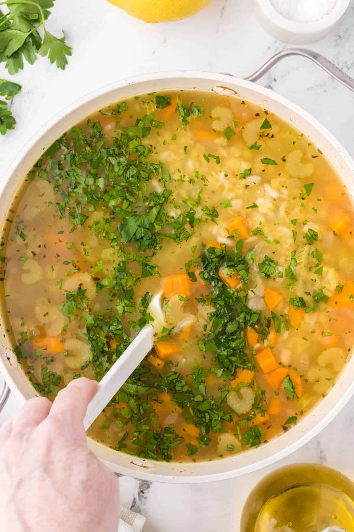 Soup stirred in a large pot is being finished with minced parsley.