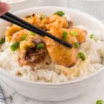 Juicy Asian shrimp in a bowl over rice. With a pair of chopsticks holding a piece of shrimp.