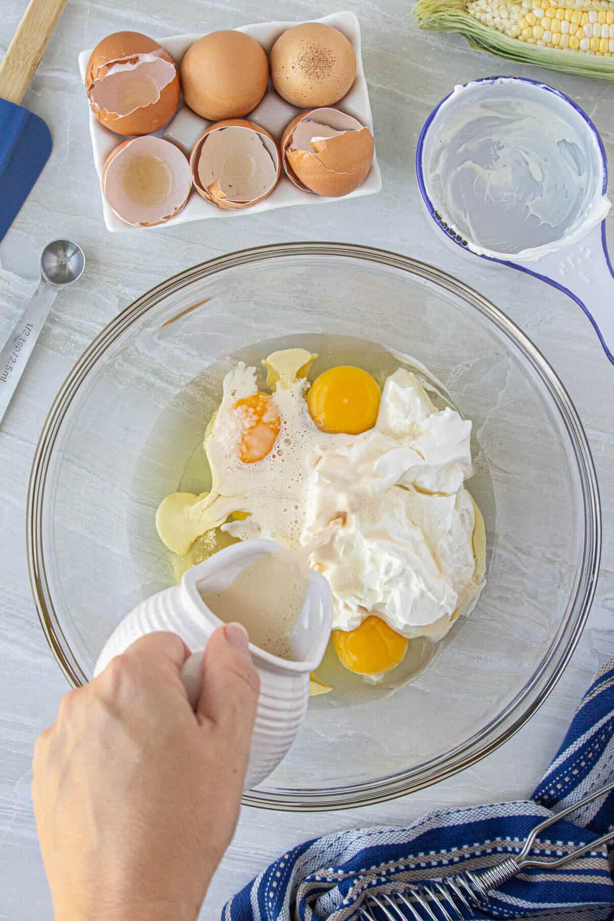 Eggs have been cracked into a bowl. Cream is being pour into a mixing bowl to whip with the eggs.