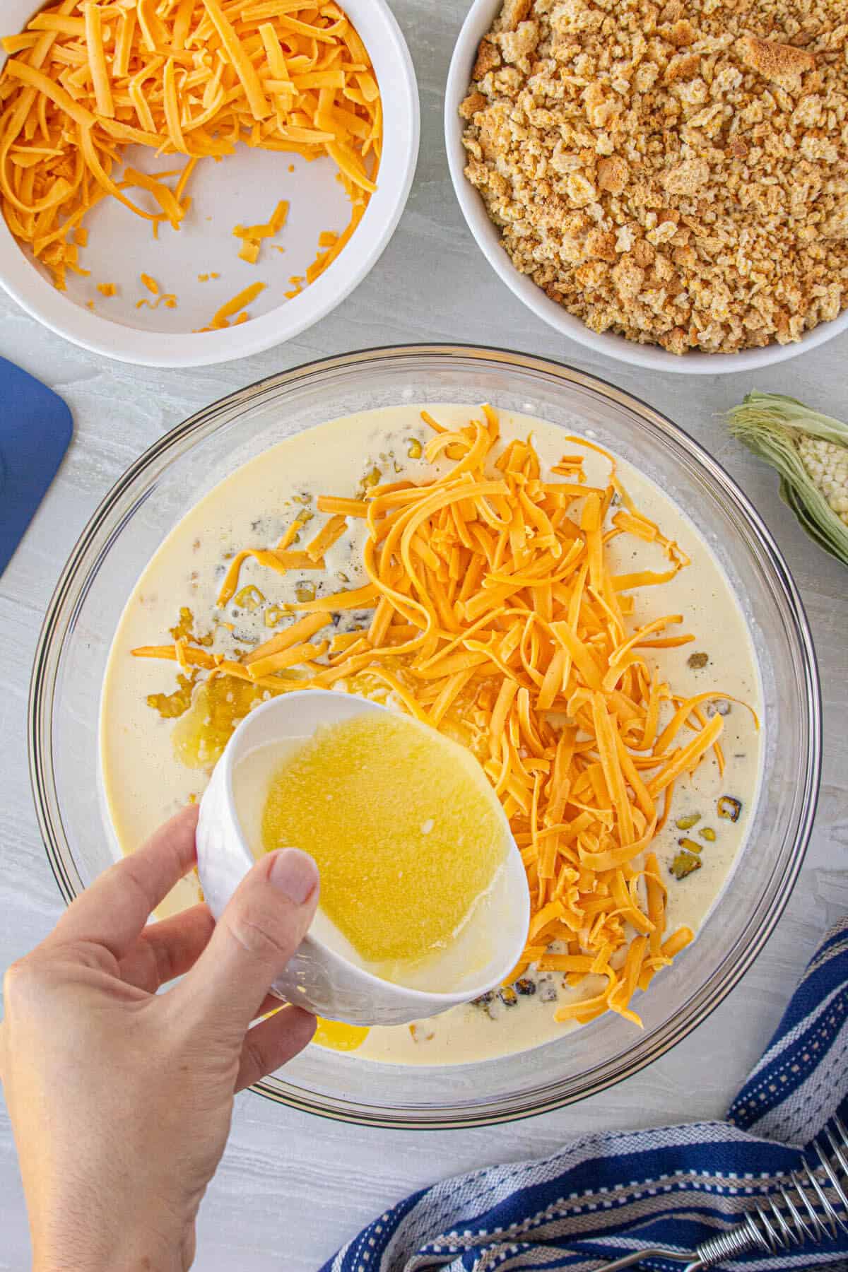 Beaten eggs in a mixing bowl. Shredded cheese and melted butter are poured into the bowl.