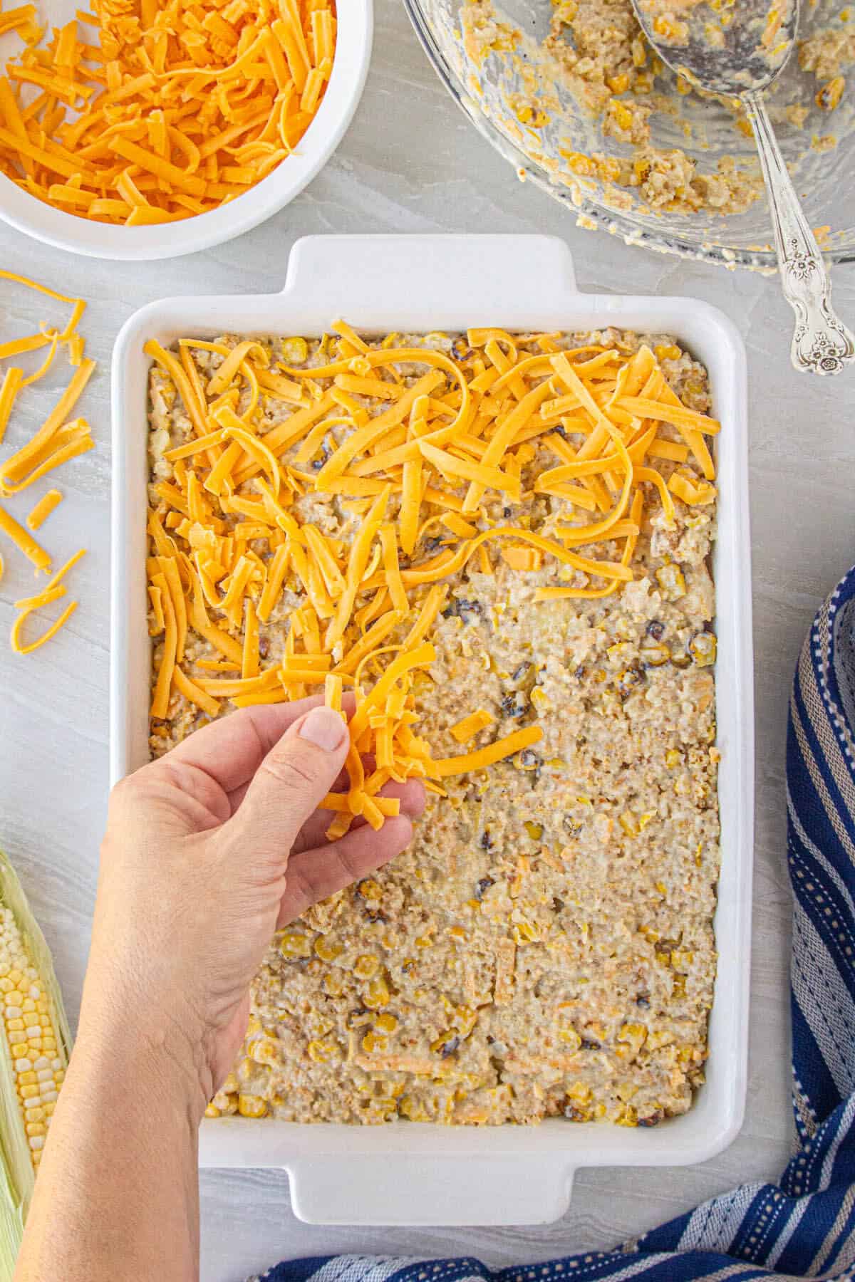 Corn casserole spread evenly in a casserole dish being topped with shredded cheese.