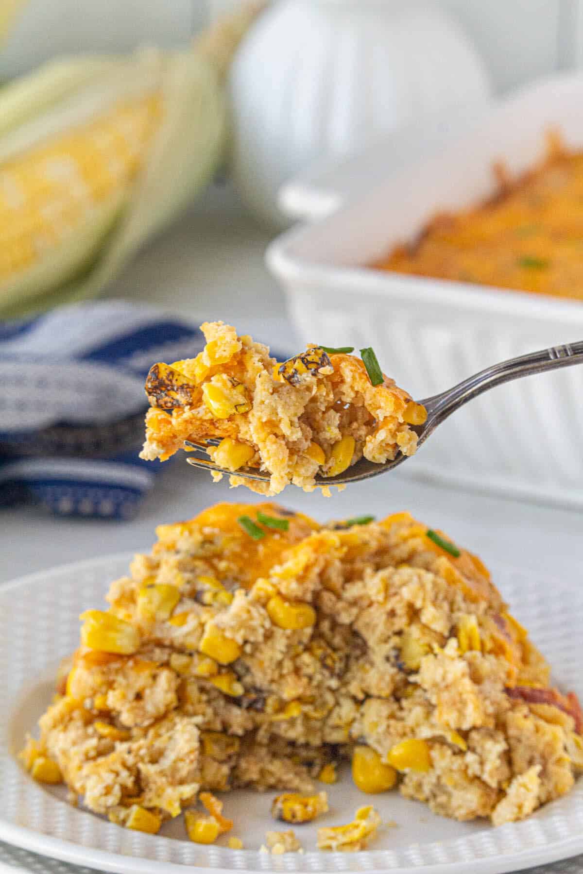 Corn casserole on a plate, with a fork holding a bite of the casserole.