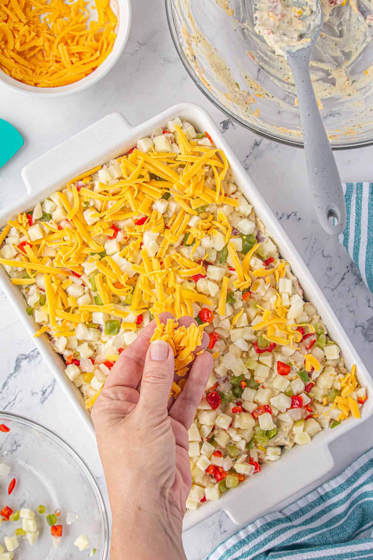 Shredded cheese being spread over the top of a hashbrown casserole.