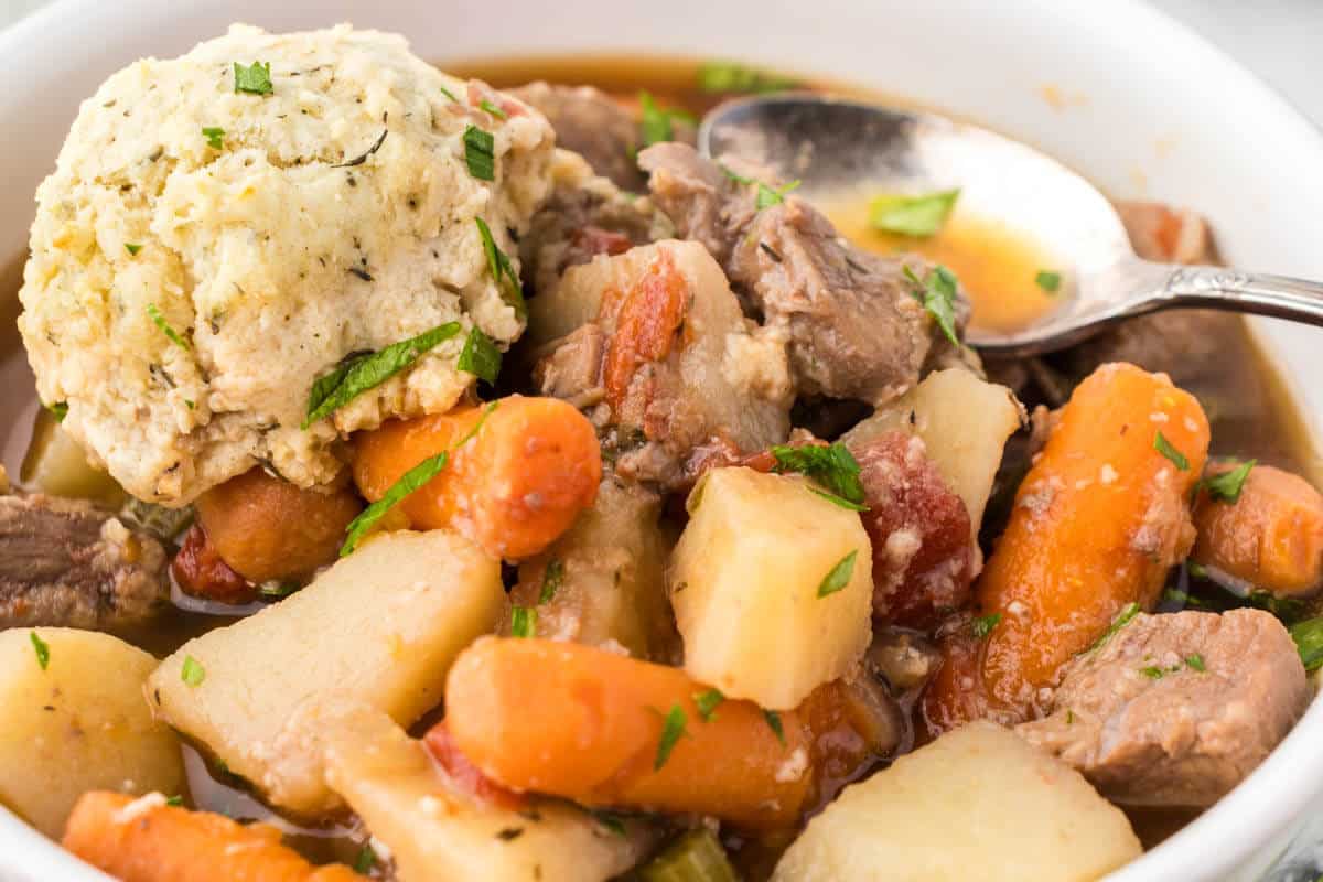 Beef stew with dumplings in a bowl with a serving spoon.