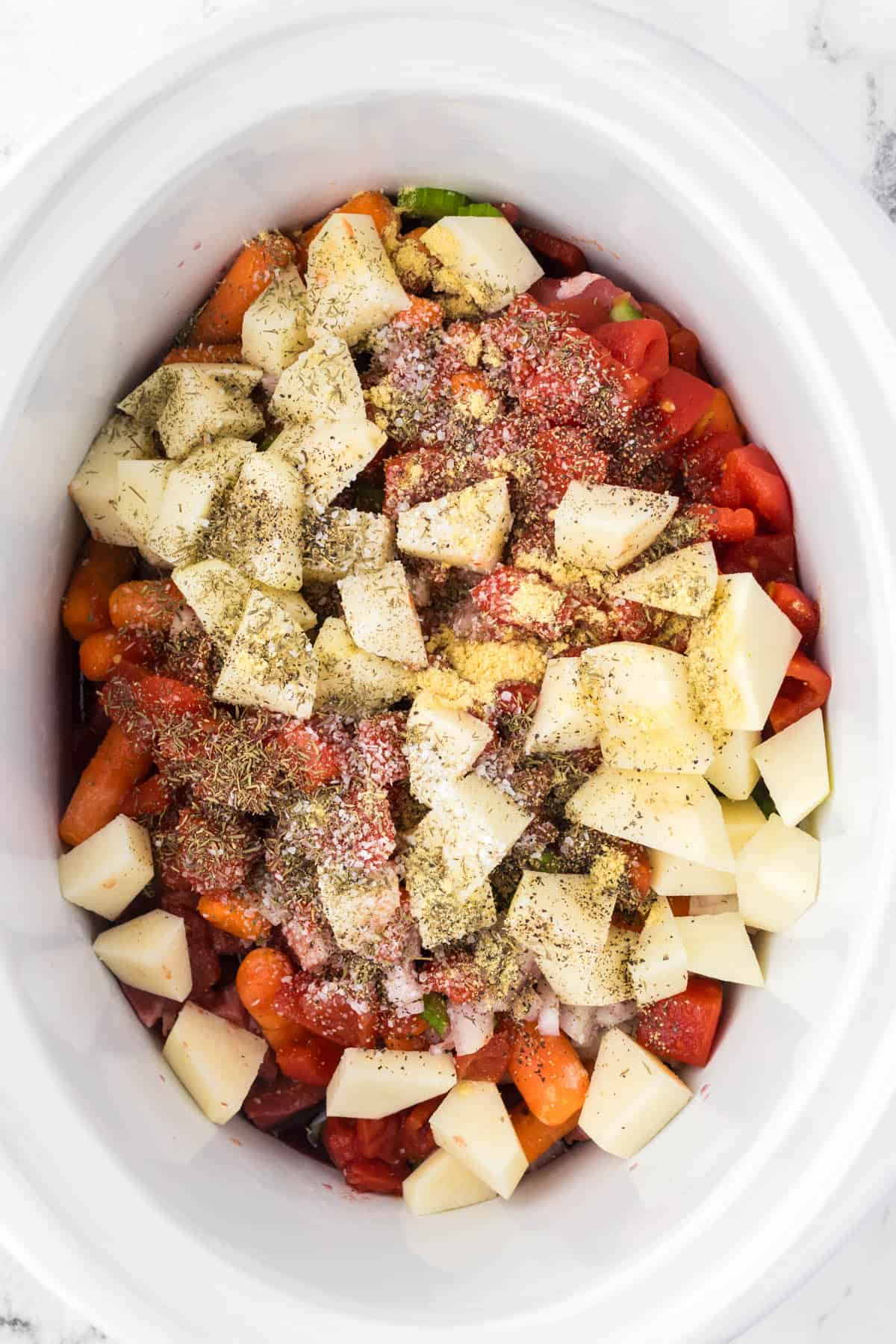 Crockpot beef stew in a slow cooker, seasoned and ready to cover and cook.