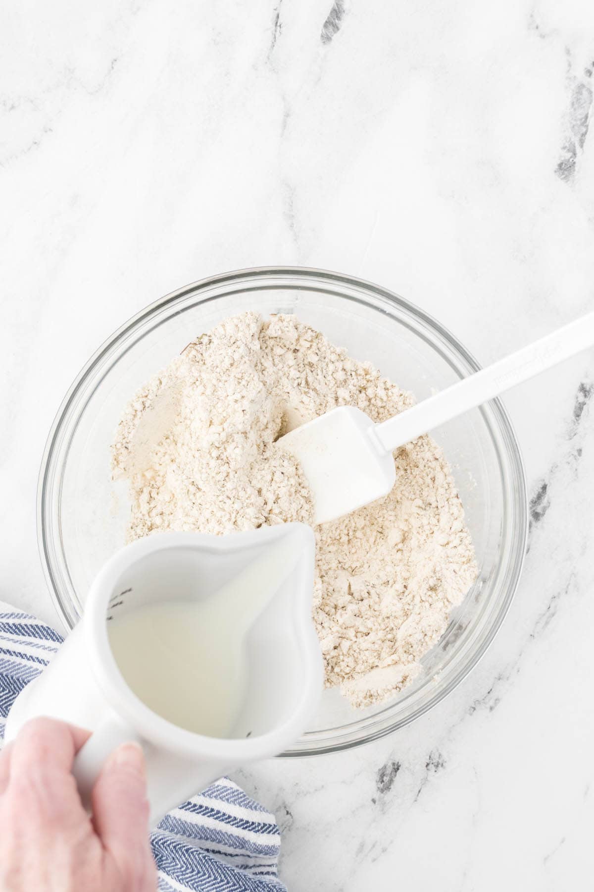 Milk pouring into a bowl of flour to make biscuits.