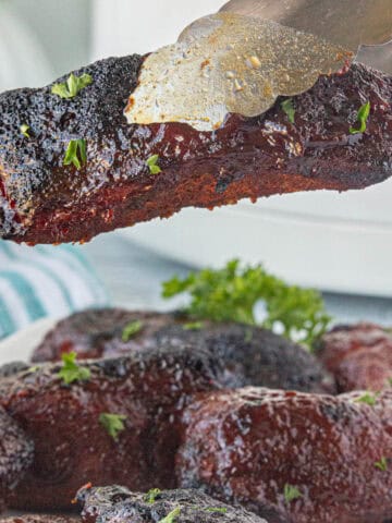 Country style ribs that have bbq'd. With serving tongs grabbing one of the ribs.