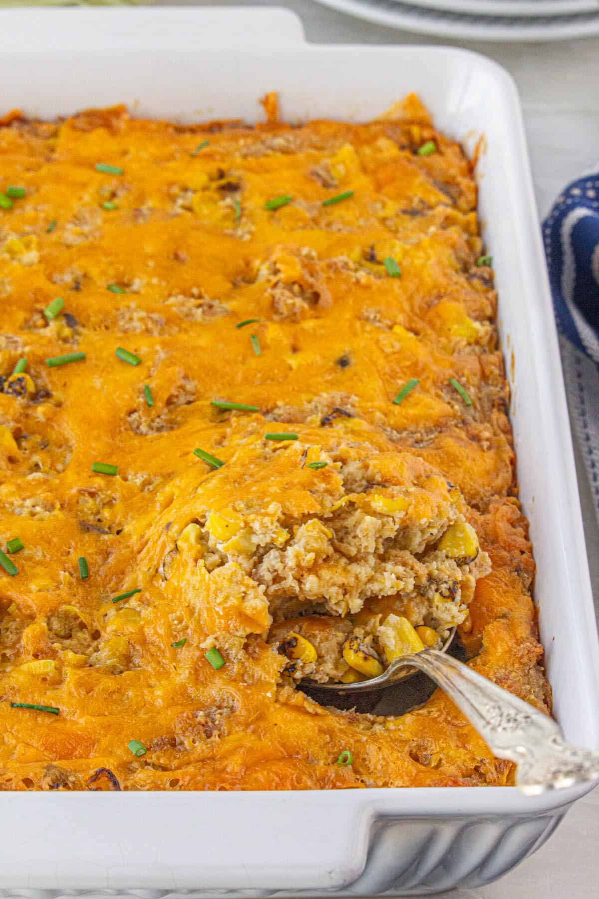 Corn casserole in a baking dish. It has been baked until hot and bubbly and the edges are crispy. A serving spoon has been placed in the casserole.