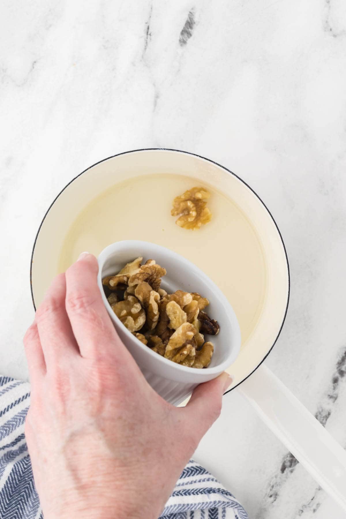 Sugar and water boiling in a pan. Walnut halves are being poured into the sugar mixture.