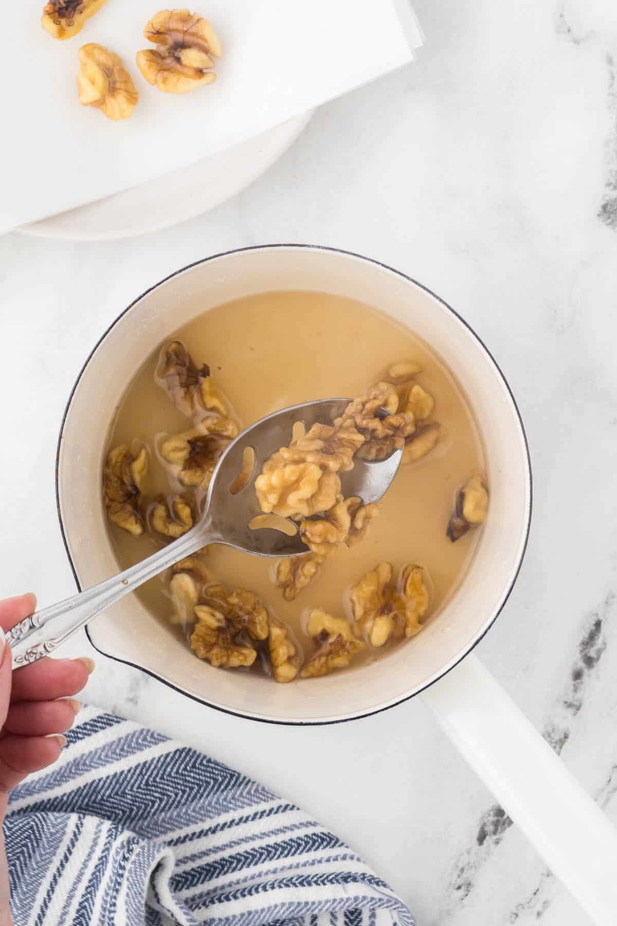 After boiling the candied walnuts, they are removed from the sugar mixture and placed on a paper towel to cool.