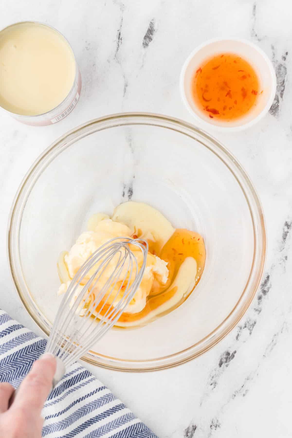 Sweetened condensed milk, mayonnaise and chili sauce in a bowl being whisked together.