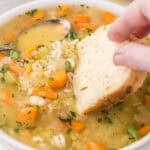 A bowl filled with lentil barley soup with a hunk of bread dunking into the broth.