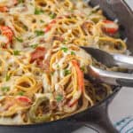 Cheesey spaghetti in a cast iron skillet with a set of tongs pulling out a serving.