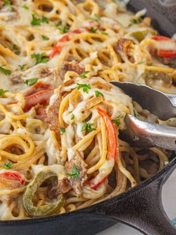 Cheesey spaghetti in a cast iron skillet with a set of tongs pulling out a serving.