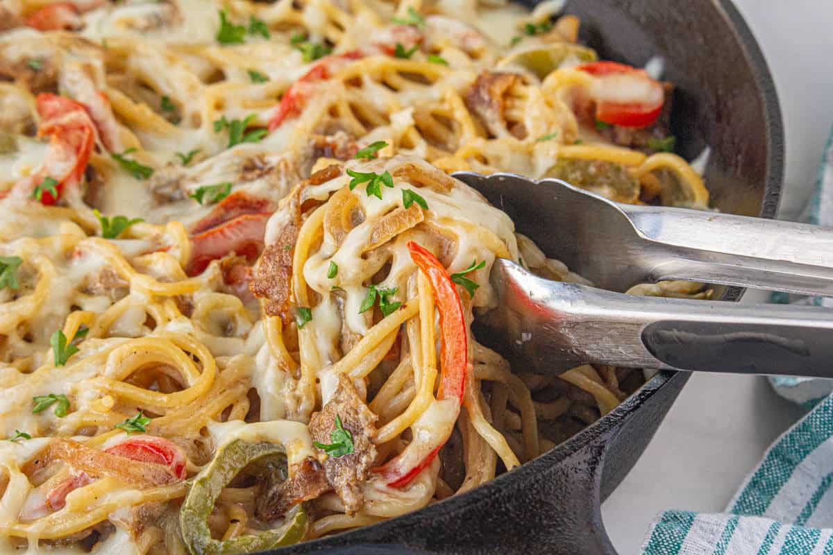 Cheesy Philadelphia Cheesesteak Spaghetti in a pan with serving tongs.