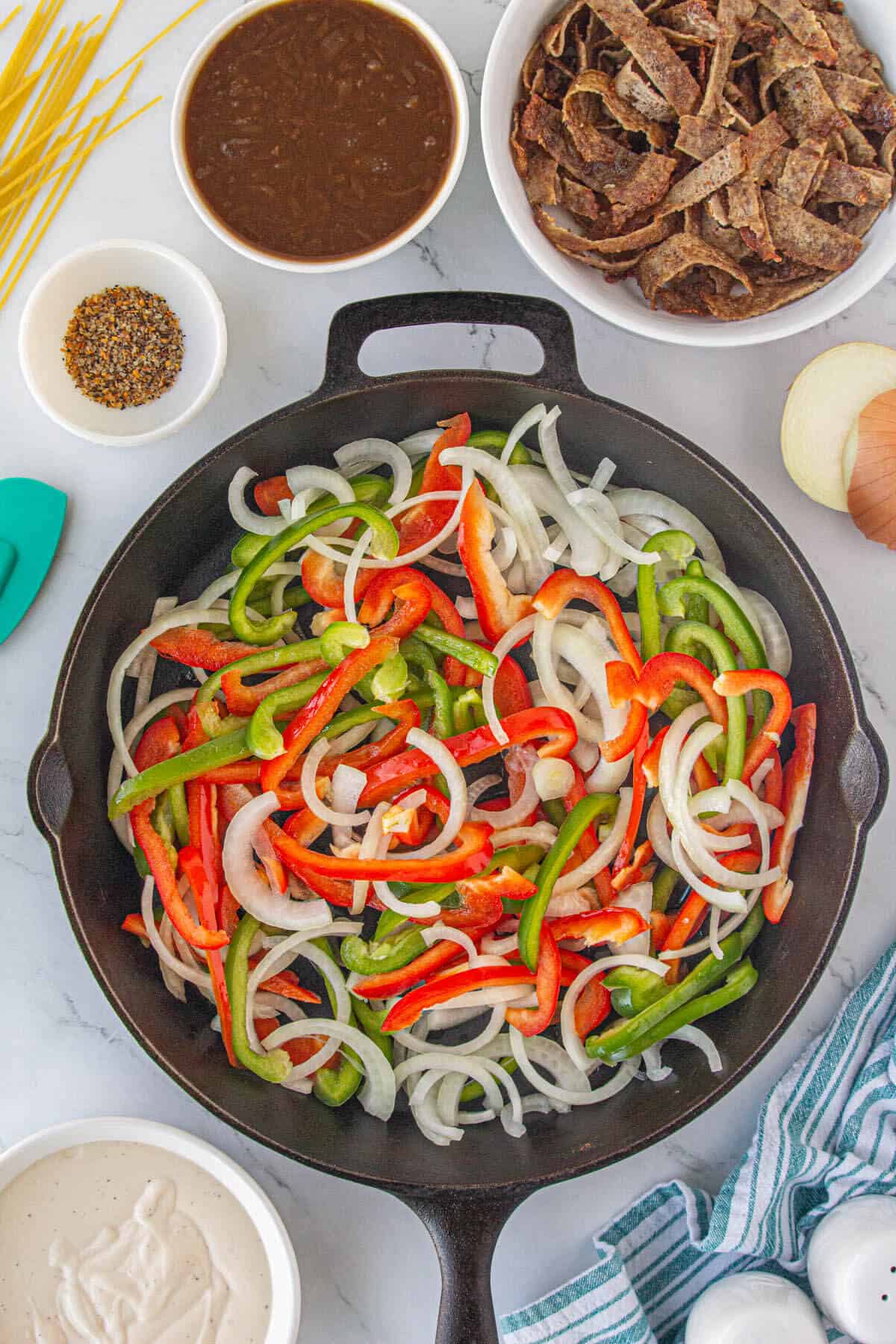 Sliced bell peppers and onions sauteing in a skillet.