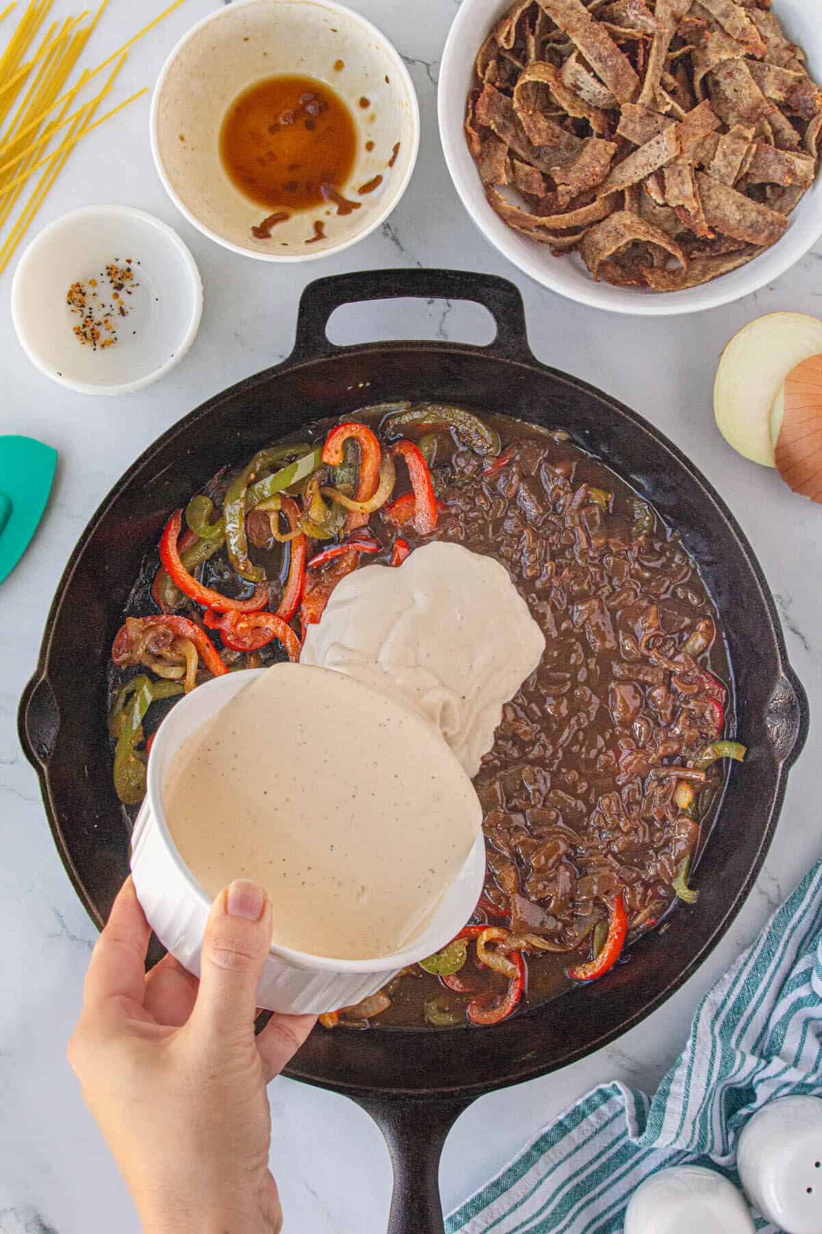 Seasoning and Alfredo sauce added to the sauteed bell peppers and onion in a skillet.