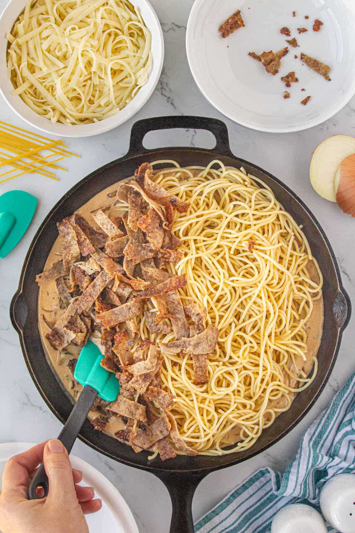 Sliced steak and cooked pasta added to a cheesy sauce in a skillet.