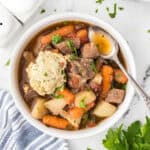 A bowl filled with beef stew, with a spoon tucked on the side of the bowl.