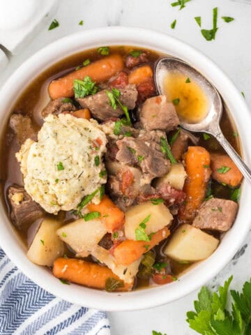 A bowl filled with beef stew, with a spoon tucked on the side of the bowl.