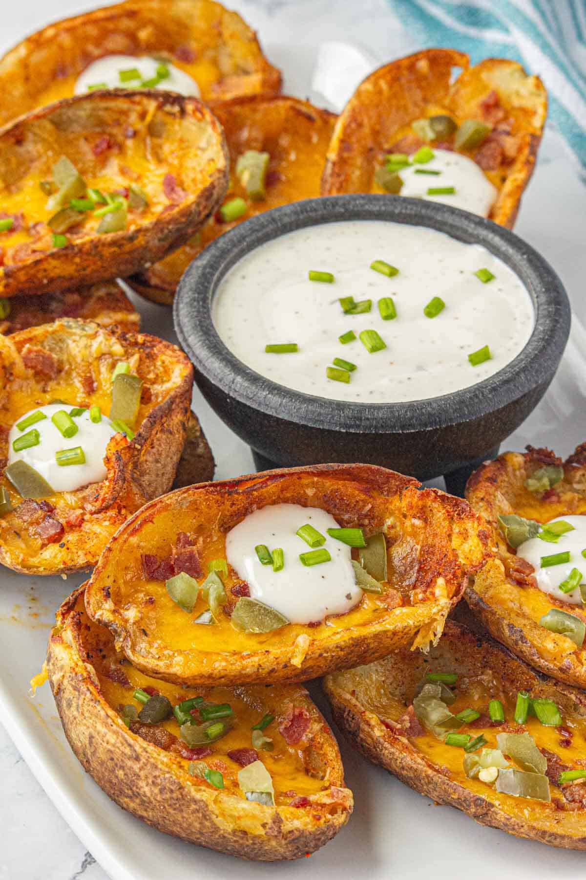 Cheesy bacon loaded potato skins on a platter, with a dipping sauce.