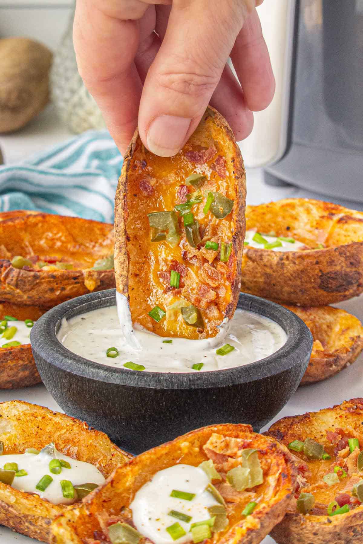 Hand dipping a crispy air fryer potato skin into ranch dressing.