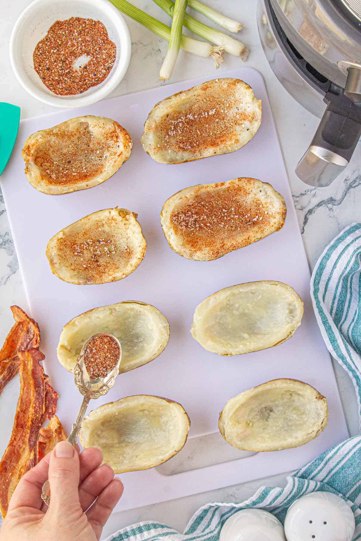 Hollowed out potato skins being sprinkled with seasonings.