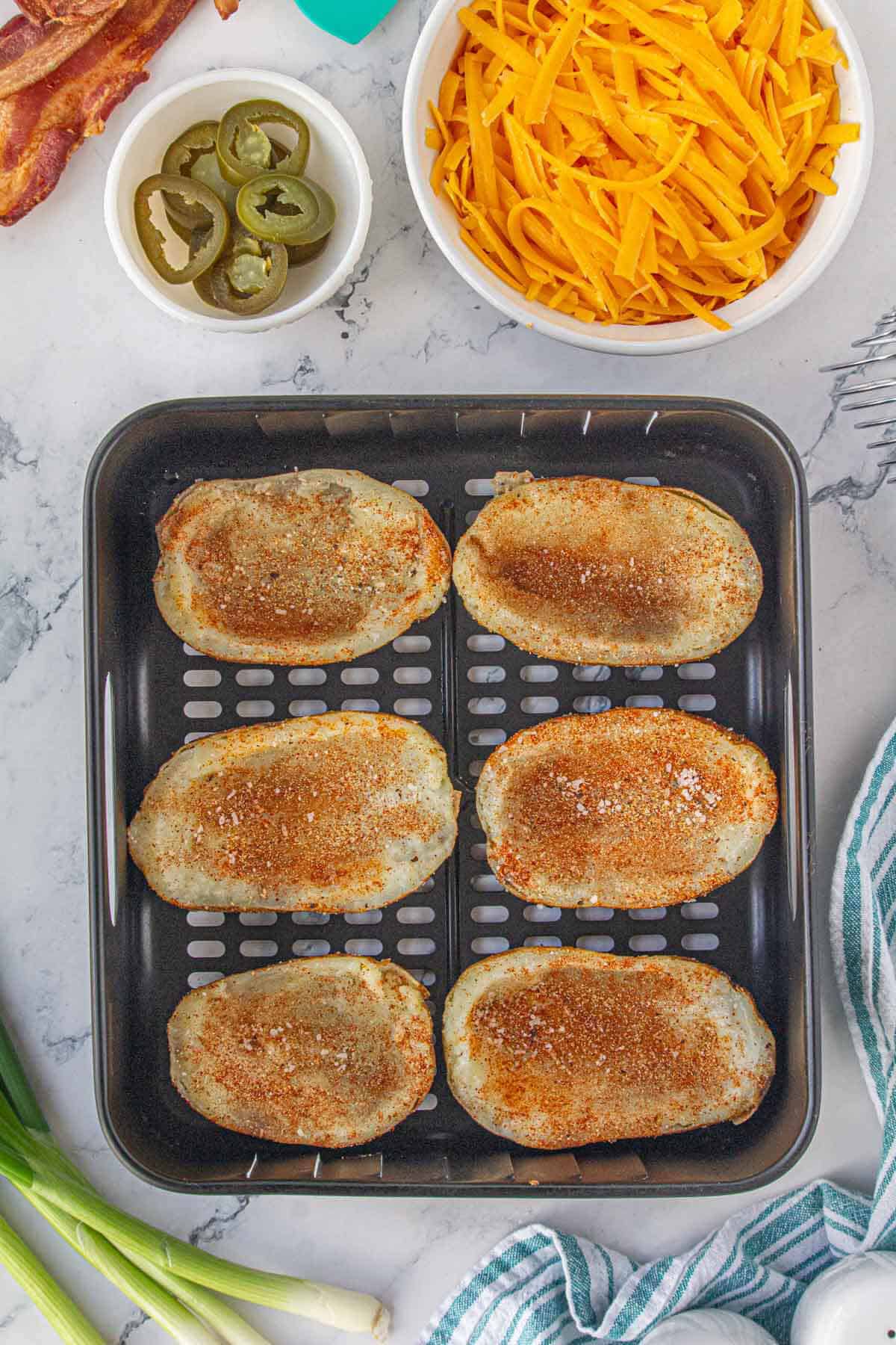 Seasoned potato skins in an air fryer basket.