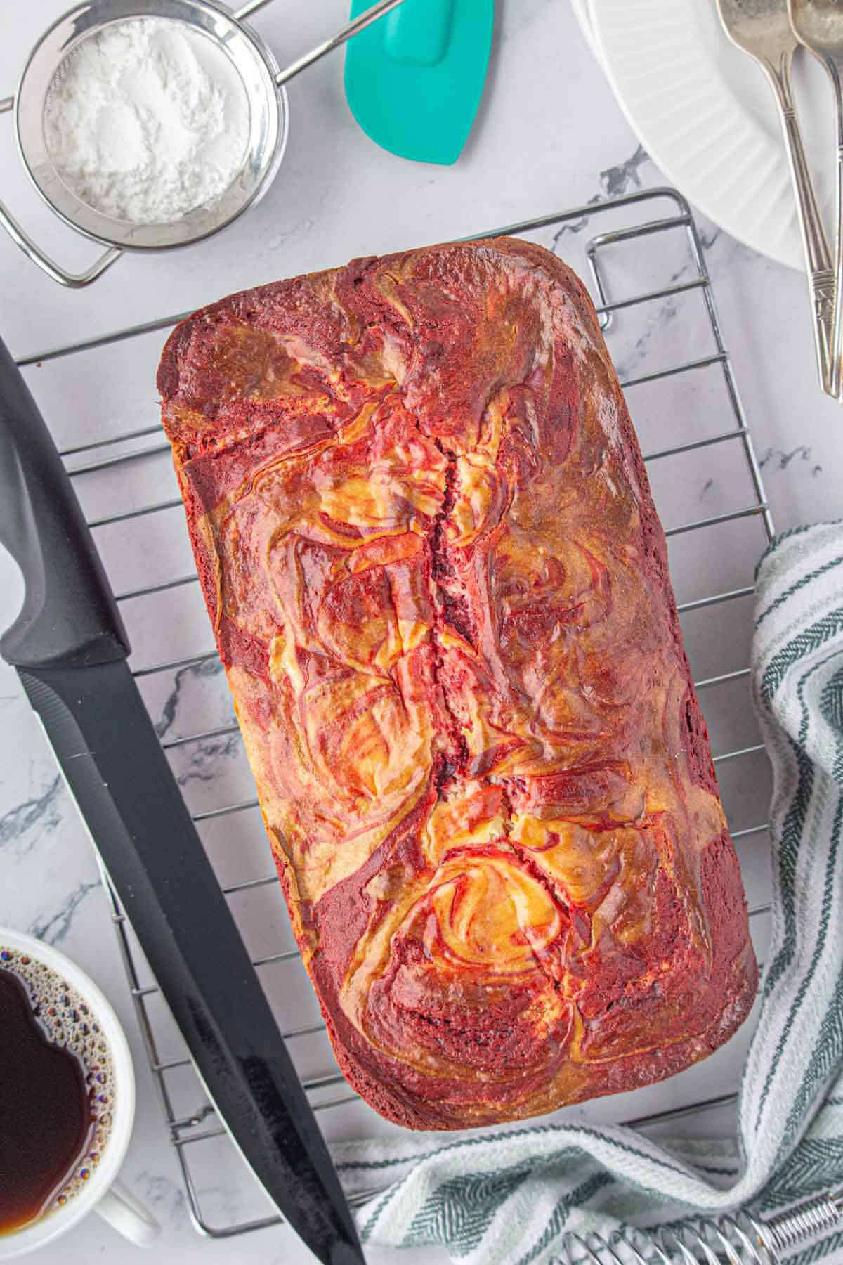 A loaf of red velvet cooling on a rack. With a knife to slice when it's ready.