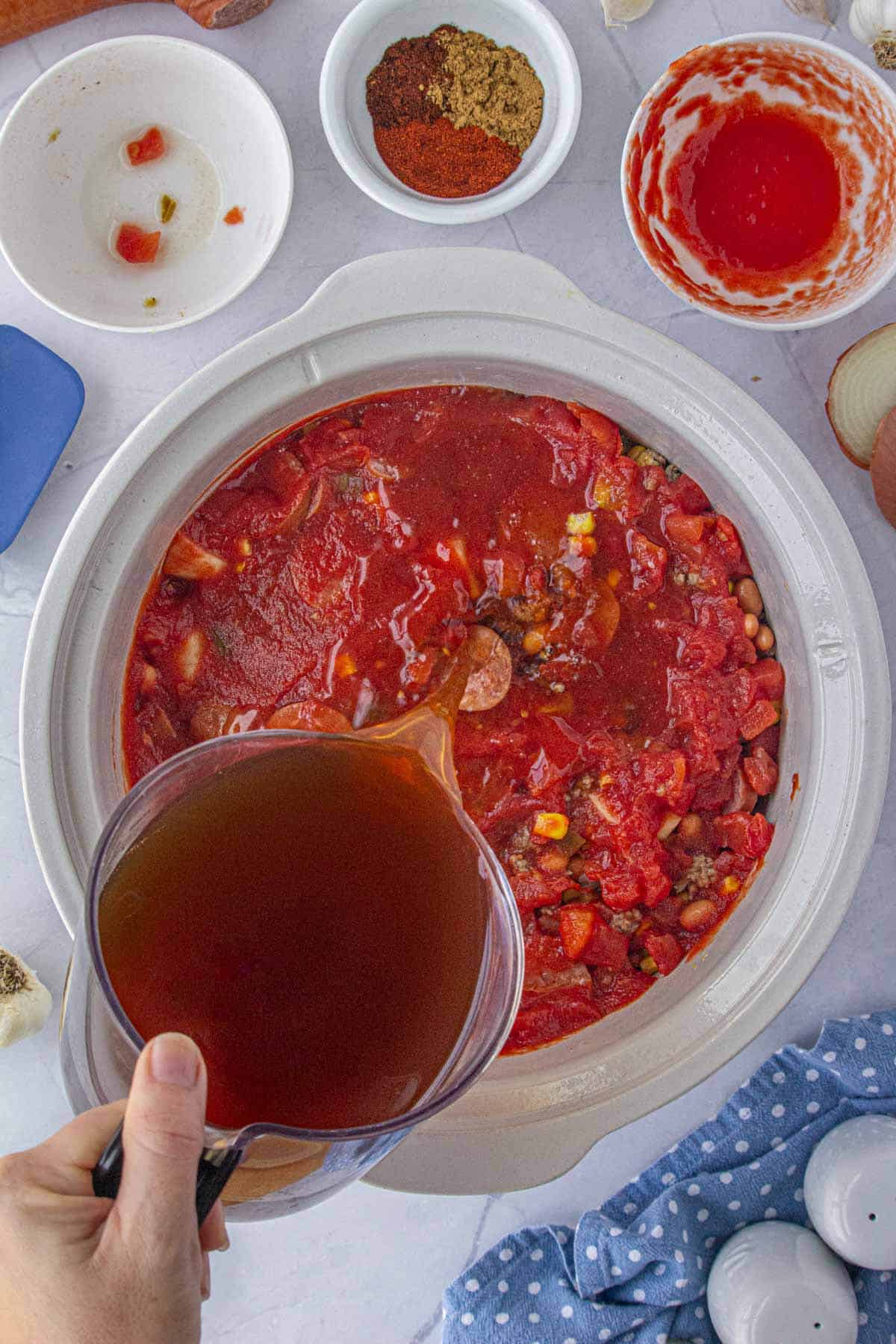 Beef broth being poured into a crockpot filled iwth stew ingredients.