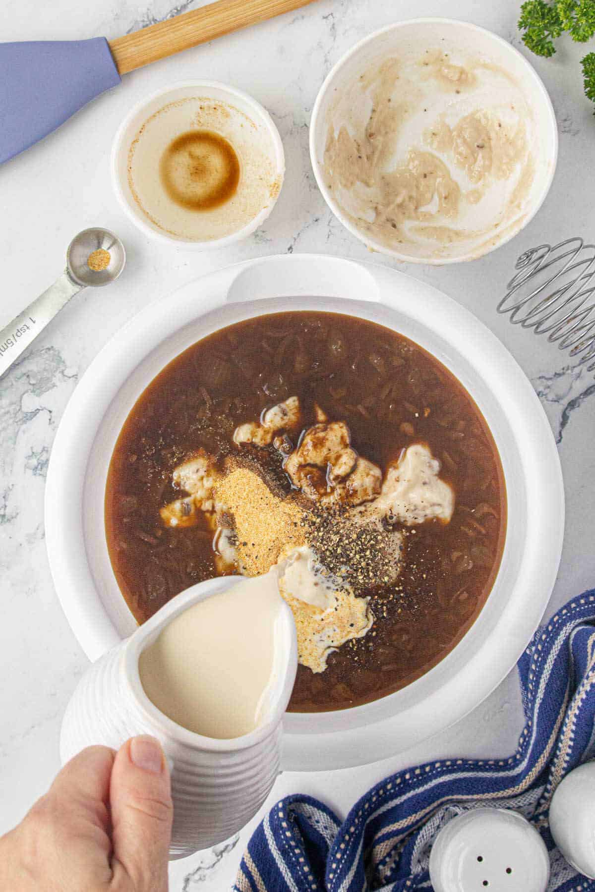 A brown sauce is being combined in large mixing bowl. There is evaporated milk being poured into the bowl.