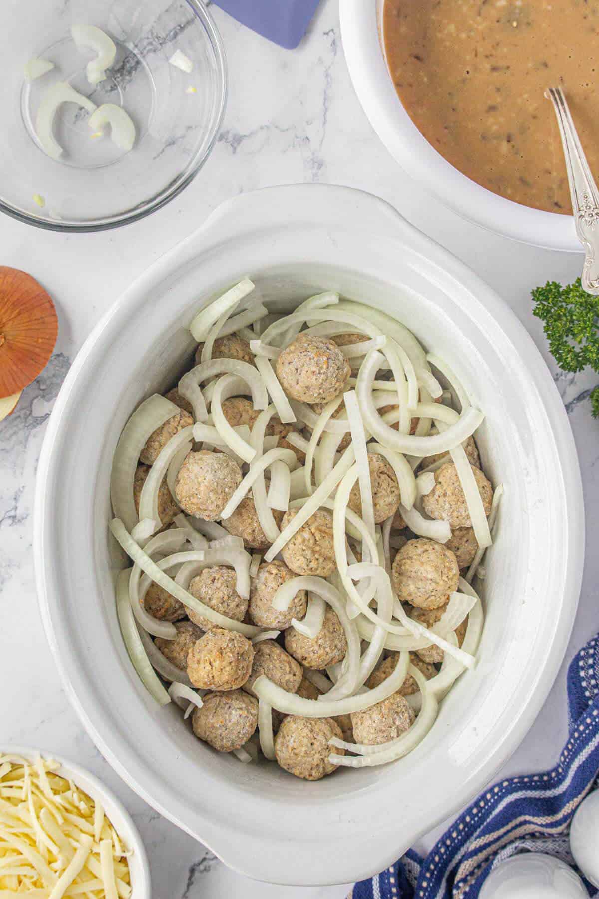 Frozen meatballs and sliced onions in a crockpot.