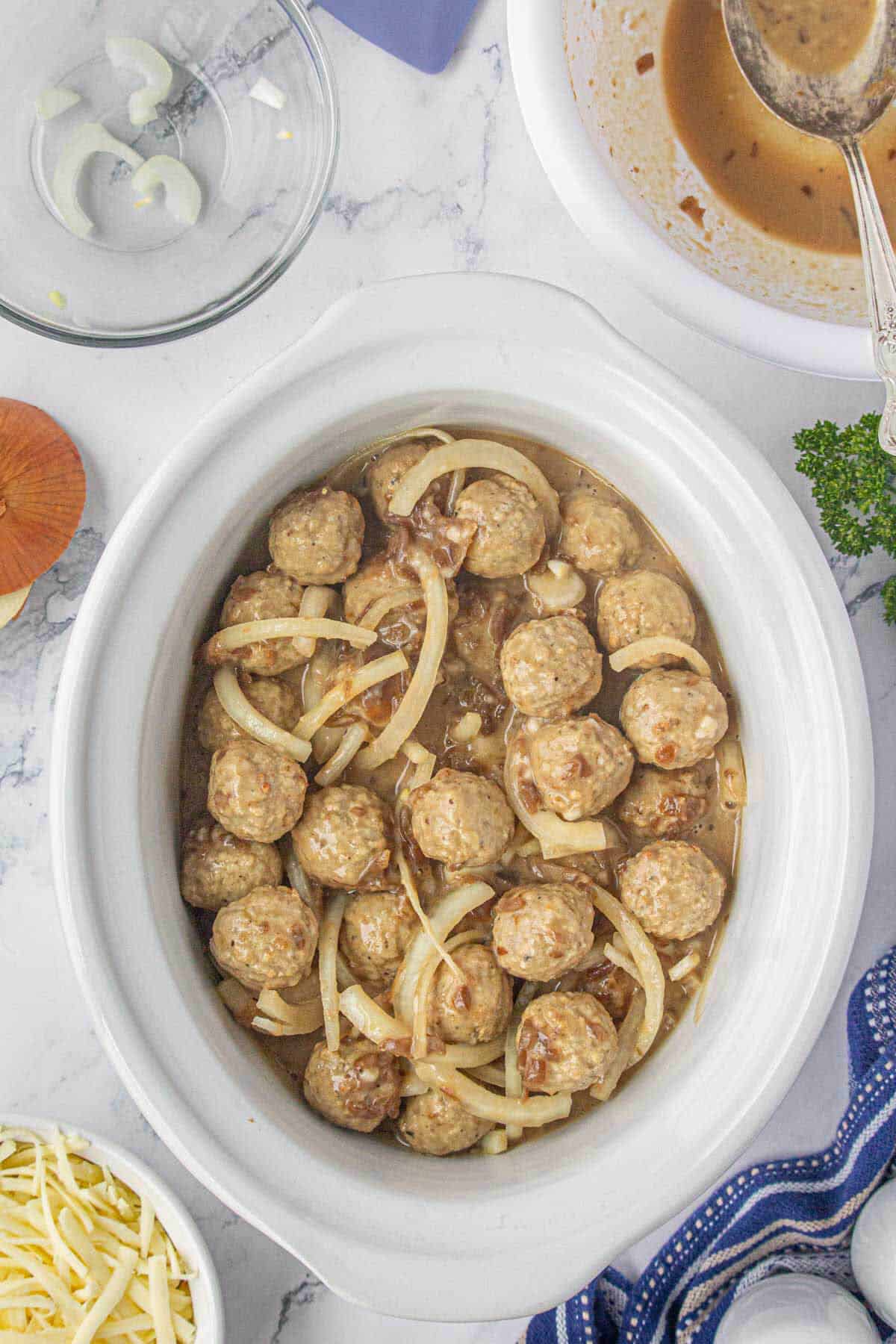 Meatballs, sliced onions and sauce in a slow cooker.