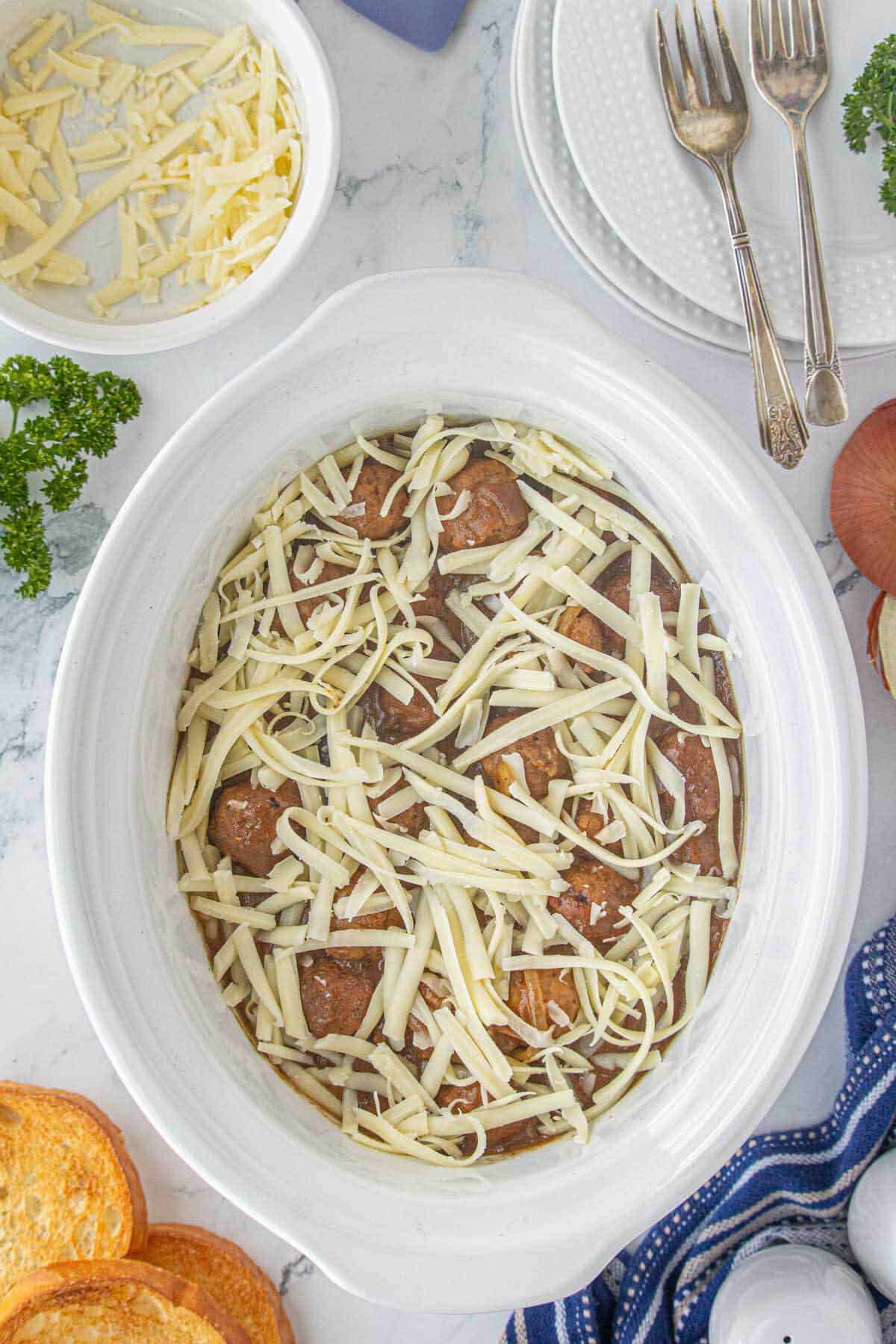 Cooked meatballs in a crockpot topped with shredded Gruyère cheese.