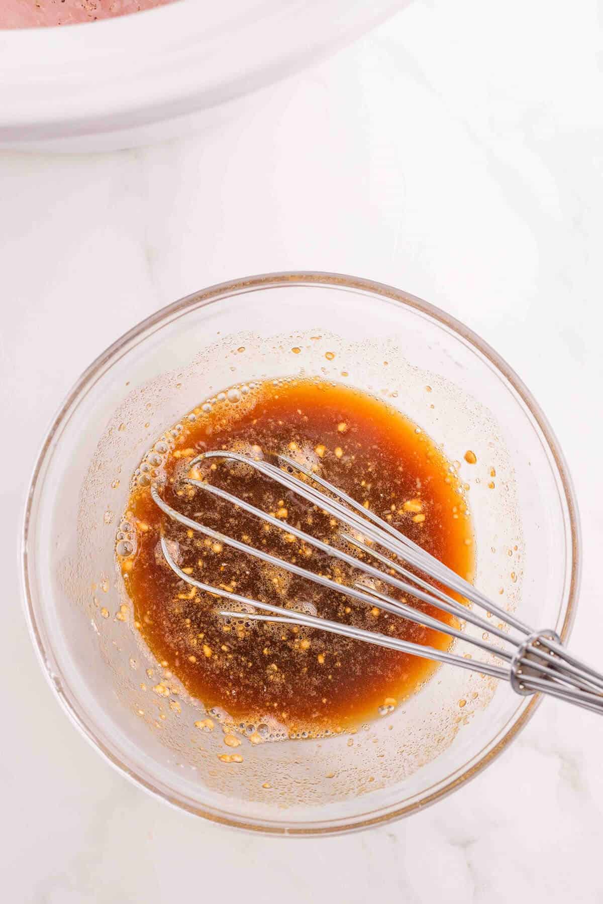 Sauce being mixed in a glass bowl with a whisk.