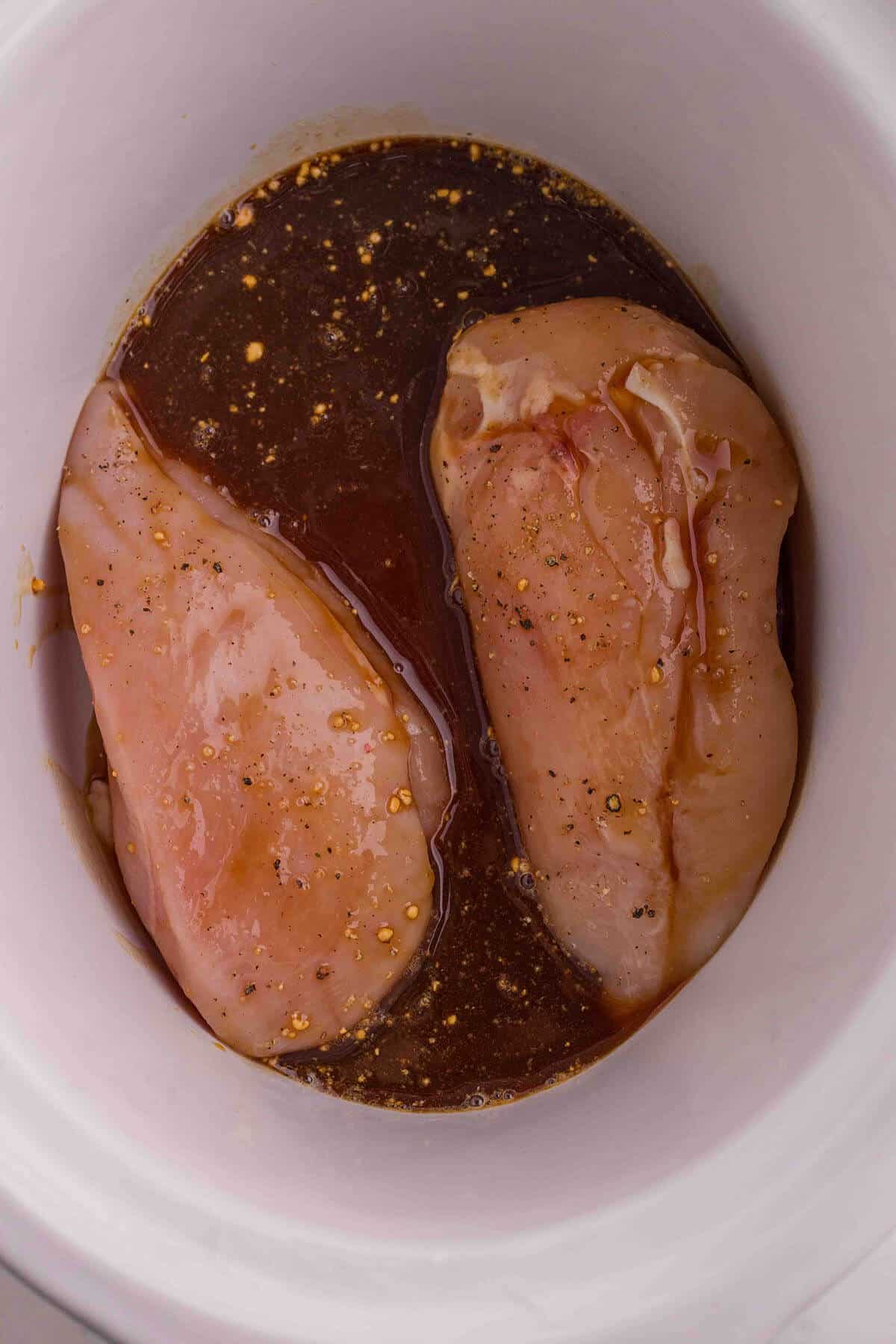 Raw chicken breast in a crockpot with sauce.