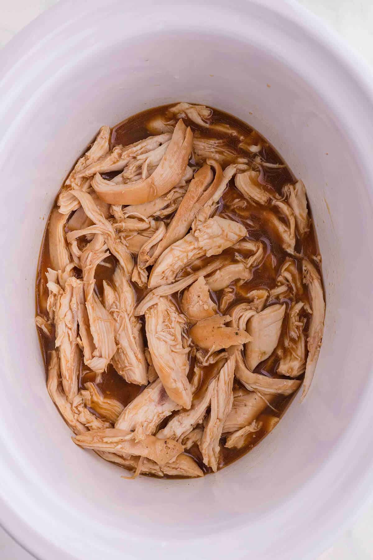 Shredded chicken in a crockpot with a tangy sauce.